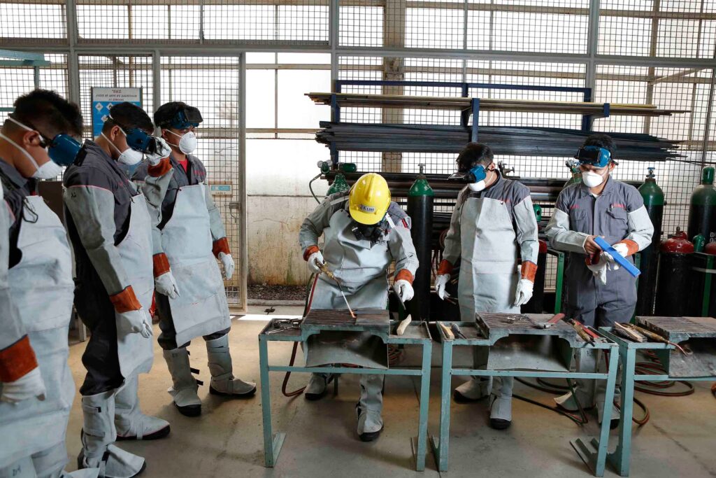 Group of factory workers in hard hats and protective gear gathered for a hands-on safety training session, reflecting adult learning theory's emphasis on real-world, applied instruction