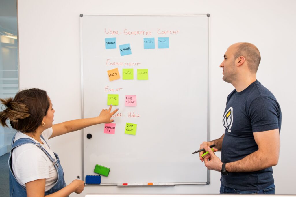 Two colleagues planning at a whiteboard together, mapping out the kind of decision-point scenario used to design training that actually changes behavior
