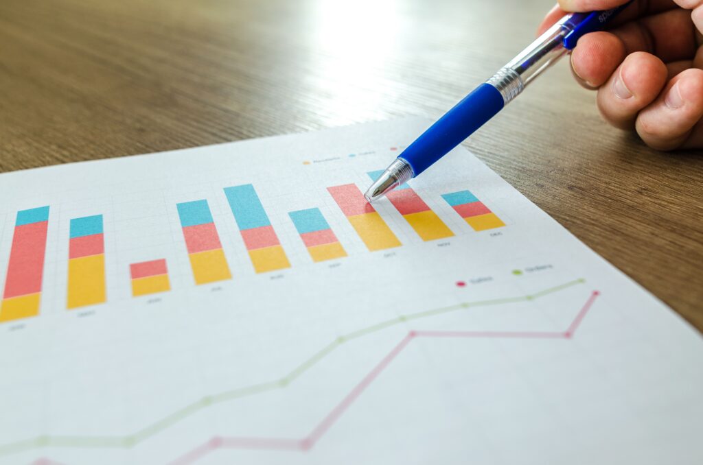 Close-up of a hand with a pen pointing to a bar and line chart on paper, the kind of data review behind training evaluation models like Kirkpatrick and Phillips ROI