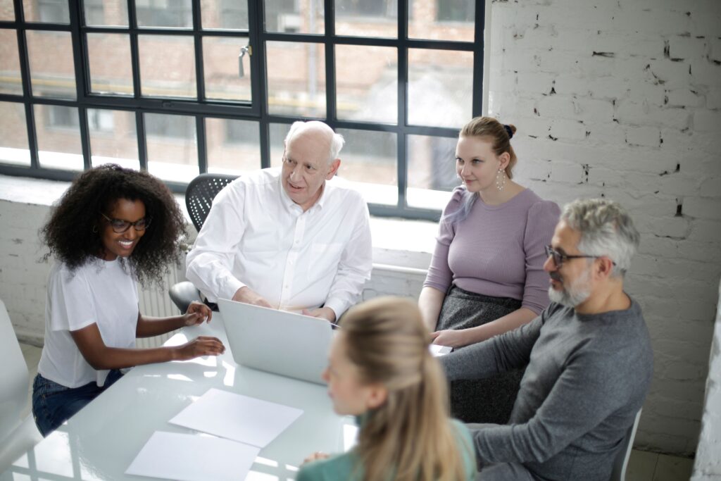 Diverse team of colleagues gathered around a table with laptops and documents in a bright, informal meeting space, discussing how to measure training effectiveness beyond completion rates