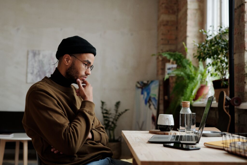 Man resting his chin on his hand while thoughtfully considering something on his laptop screen, the kind of engaged weighing of options that strong scenario-based learning creates