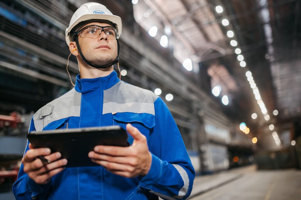 Factory worker in safety gear checking a tablet on the production floor, the kind of quick, in-the-flow-of-work moment microlearning for employee training is built for